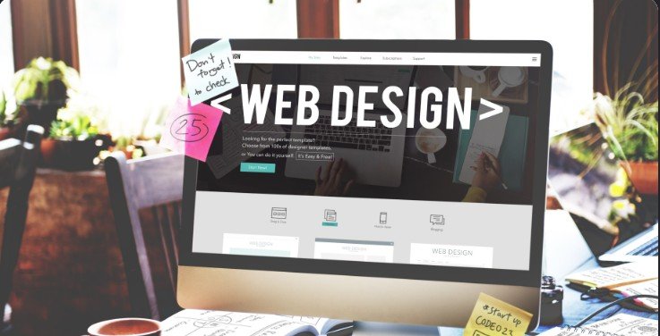 Desktop monitor showing a web design page, with sketches and notes on the desk